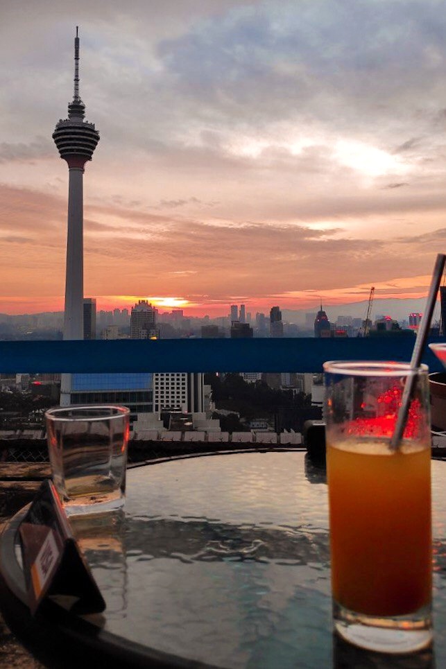 A view Kuala Lumpur Tower during dusk matching with the colour of orange juice paired with a metal straw.
