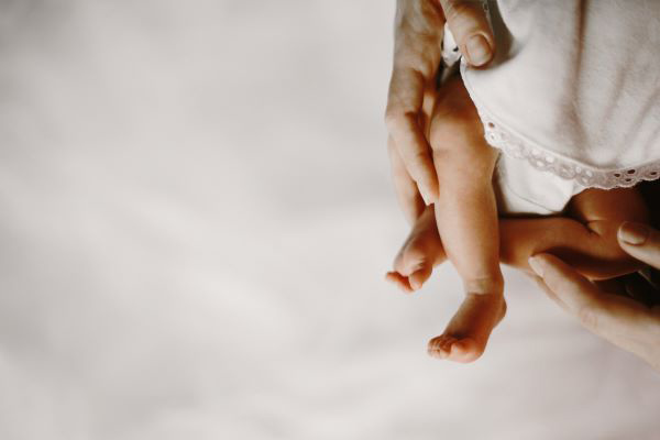 newborn; a persons hands holding the tender legs of a newborn