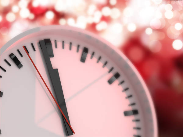 12 O’clock, indicating the end of 2020, Happy New Year 2021. Clock showing one minute until midnight, with a blurry red lights in the background.