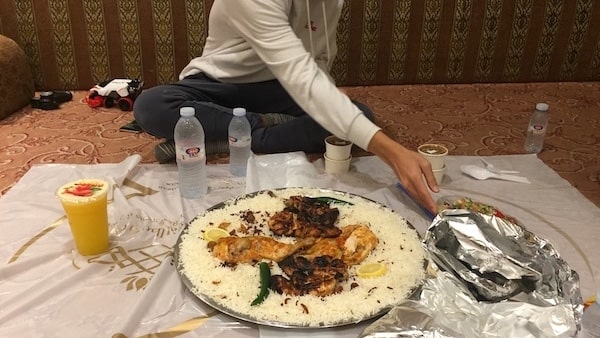 A photo of a traditional Saudi dish  called kabsa, served in a large tray, where everyone sits on the floor and eat together.