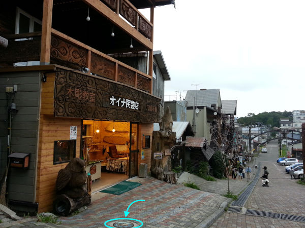 Manhole alert! Ainu souvenir shop with big wooden owl carving. In front of the owl is Lake Akan's colourful manhole cover.