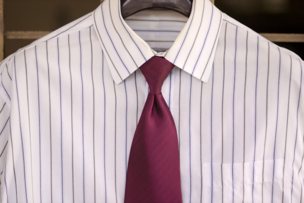 Solid stripe shirt with white base and alternating blue and black bold vertical stripes on a hanger, with a conservative solid maroon tie.