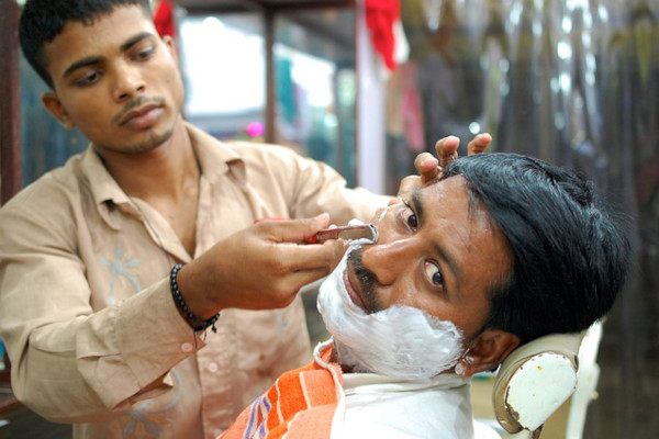 A customer having an full fledged wet shaving treatment with a professional barber. His beard being lathered evenly, and the barber carefully shaving with a straight razor.