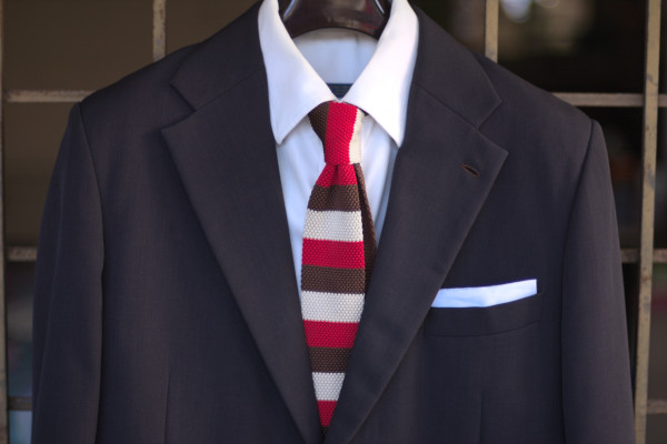 Close-up of the chest, showing a three-tone, brown-red-beige segmented tie on a charcoal suit jacket and solid white shirt.