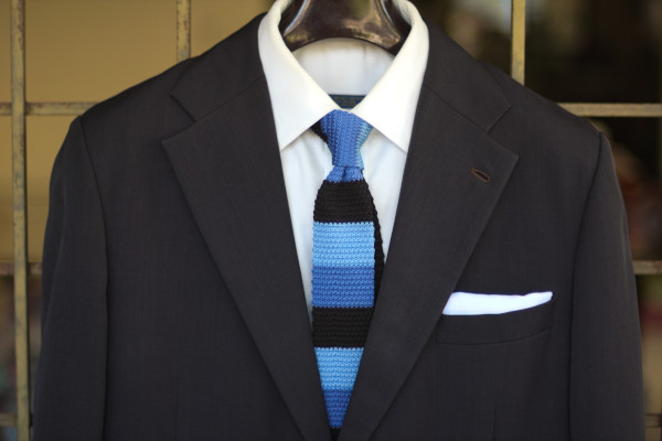 Close-up of the chest, showing a three-tone, blue-on-blue segmented tie on a charcoal suit jacket and solid white shirt.