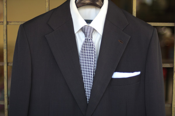 Close-up of the chest, showing a black and white houndstooth knit tie on a charcoal suit jacket and solid white shirt.
