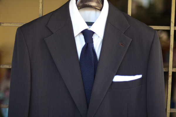 Close-up of the chest, showing a solid navy knit tie on a charcoal suit jacket and solid white shirt.