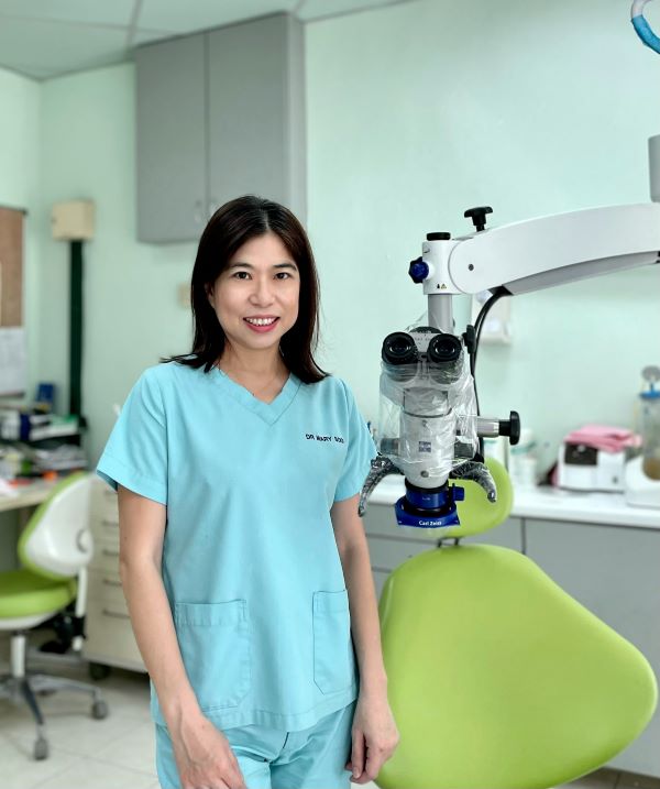 Dr Mary Soo, stands beside a green chair and dental microscope. 