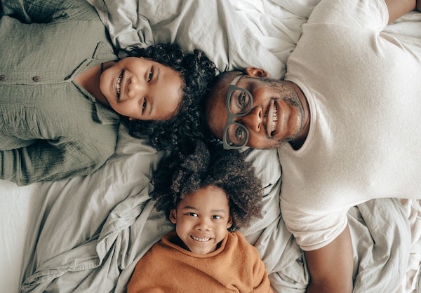 A family of three laying down with a smile together on a bed facing the camera signifying the evolution of sleep adulthood. 