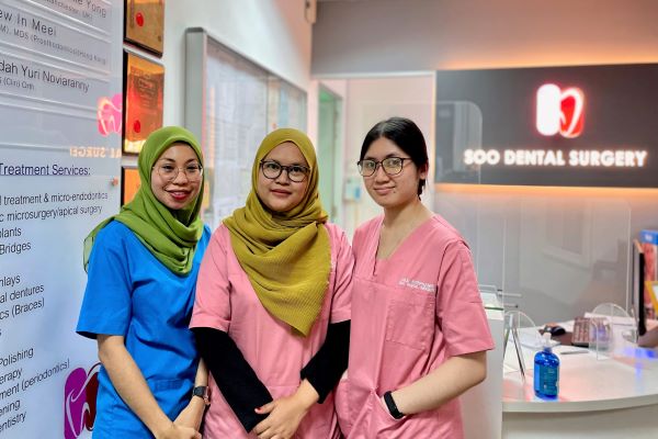 Three dental nurses stand in front of the reception counter of Soo Dental Surgery.