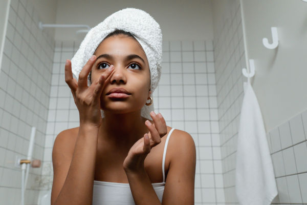 Girl in a white tank top, with hair wrapped up in a towel applying face cream in a white tiled bathroom.
Being someone with sensitive skin means my skincare routine is also as different.