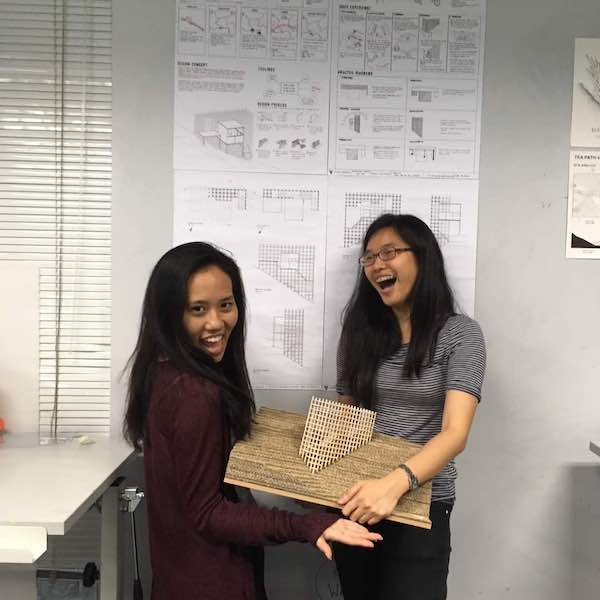 Clara and her friend, Joy, smiling to the camera while holding up an architecture model.