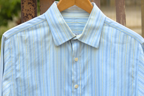 Overall image of a light blue shirt with alternating blue, yellow and white vertical stripes.