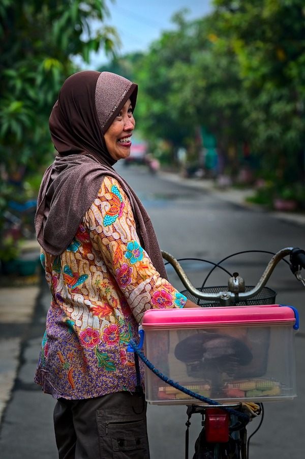 An old woman walking her bike while wearing a batik in Asia. 