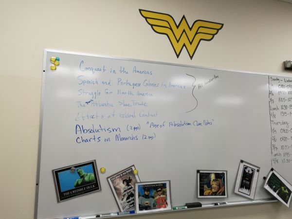 Learning history in a classroom with whiteboard decorated with DC characters.