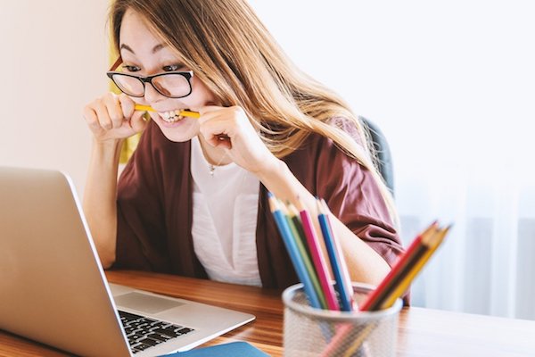 woman chewing pencil in front of laptop