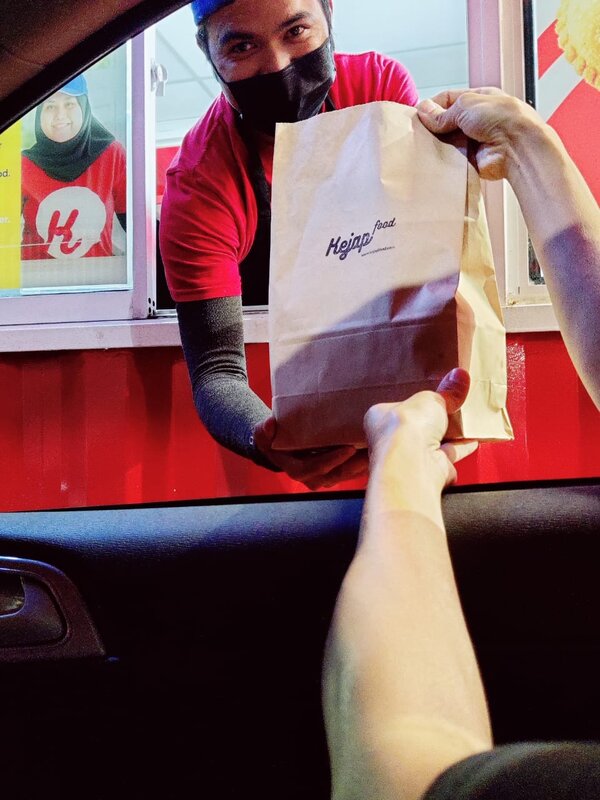 A drive-through attendant passing packed meals in a paper bag from the kiosk window