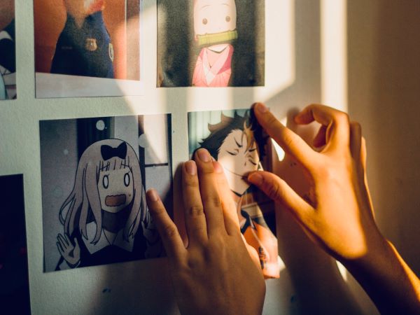 Two hands pasting an anime picture on the wall. 
