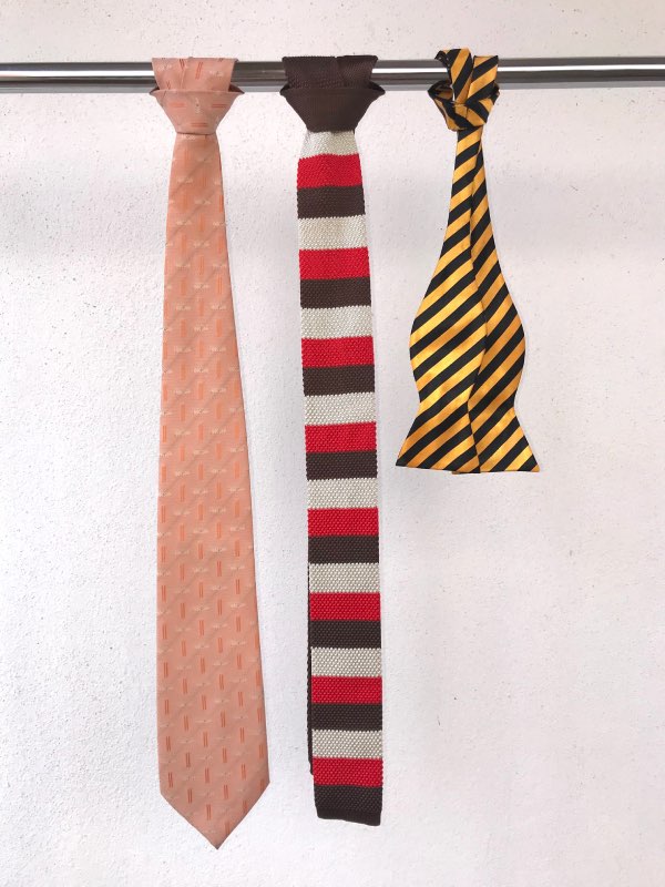 Three ties, one peach coloured tie with small repeating pattern. One knit tie in block autumn colours. One bow tie in black and yellow regimental stripes.