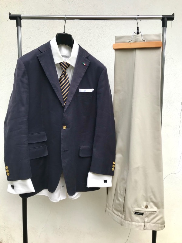 Blazer ensemble, with a solid white dress shirt, navy and gold regimental stripe tie, white pocket square, and navy cufflinks. Bottom half is that of a beige dress trousers.