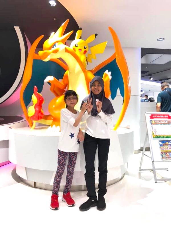 Two girls standing in front of a Pokémon statue. 