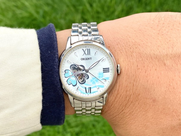 Close-up of the Orient Clover, a typical ladies' watch, on the wrist. Paired with an off-white, cotton sport jacket, and a navy roll-neck jumper.