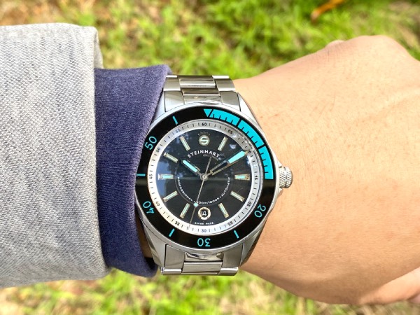 Close-up of the Steinhart Ocean 2 diver, as worn on the wrist. Here it's paired with a light grey jacket and dark blue/grey jumper sleeve. This showcases how this bulky diver can't slip neatly underneath the sleeves.