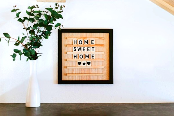 A decorative plaque hanging on the wall, saying "Home Sweet Home", and a white vase, with a green plant next to the plaque.