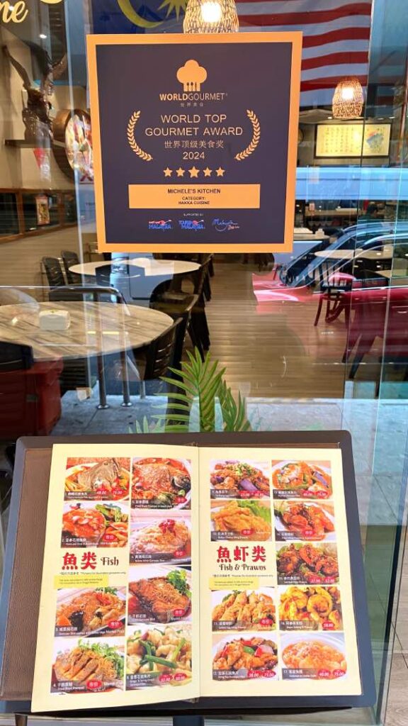 Outside view of the front door, showing the World Top Gourmet Award 2024, for Hakka cuisine. Directly below that is menu on a stand.