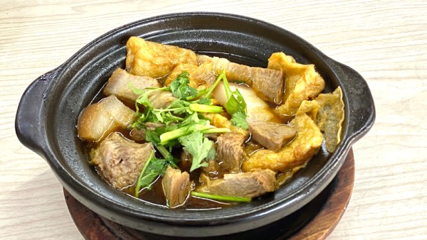Close-up of a traditional stewed bak kut teh in a claypot. Cuts of pork, beancurd sheets and garnishing of Chinese parsley are visible.