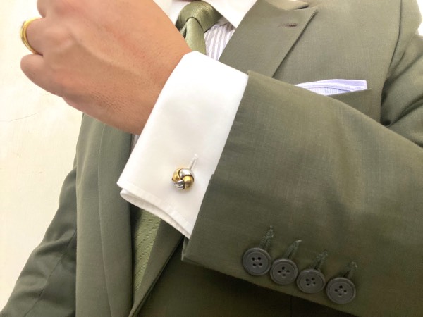 Close-up of a cuff link, fastening the two ends of the fold-over, double-cuffs together. With a suit jacket worn over top, and a pocket square.
