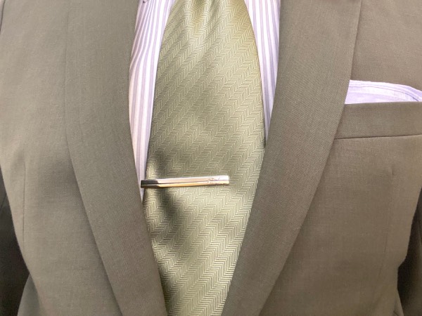 Close-up of a tie clip, fastening the tie to the placket of the shirt. With a suit jacket worn over top, and a pocket square.