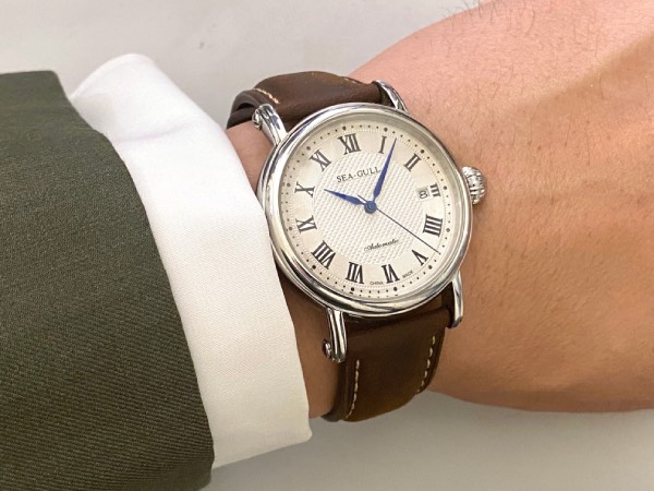 Close-up of the Sea-Gull M186S watch. A stereotypical dress watch, with Roman numerals printed on all the hour markers. Worn on the wrist, under a solid white, double-cuff, and a suit jacket sleeve cuff.