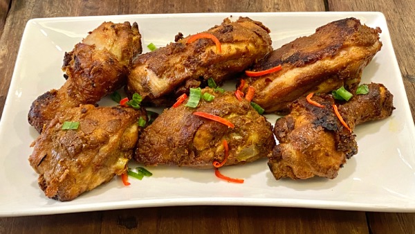 A dish featuring Sri Nyonya's Inche Kabin, with six pieces of neatly laid out, deep fried chicken. It's garnished with contrastingly colourful cut chilli and spring onion.