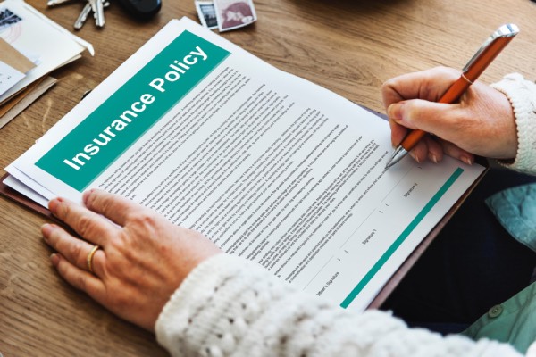 Close-up of a stack of insurance policy, being signed by the policy owner. Life insurance usually covers for accidents, diseases, and especially death.