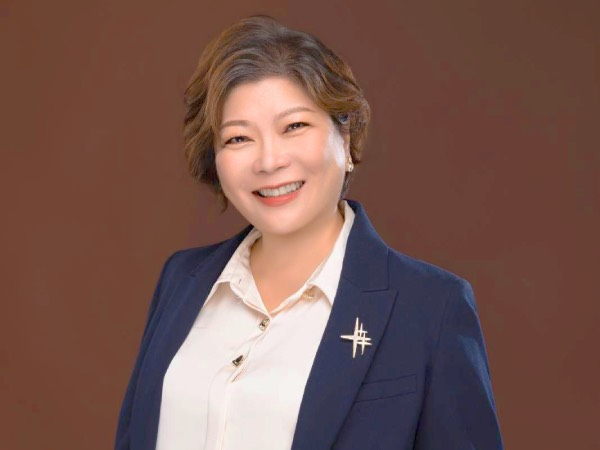 A studio taken, half-body profile photo of Sharon Lee, dressed in a navy jacket and white blouse.